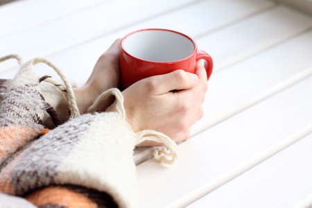 red mug in his hands and a warm blanket for restの写真素材