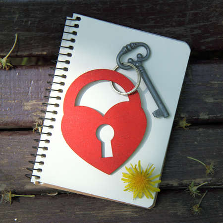lock key symbol and heart on a notebook with a pencil top view / unusual love letterの写真素材