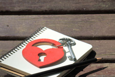 heart symbol in the form of a padlock with key on a background of a notebook with a pencil on a wooden background / love notesの写真素材