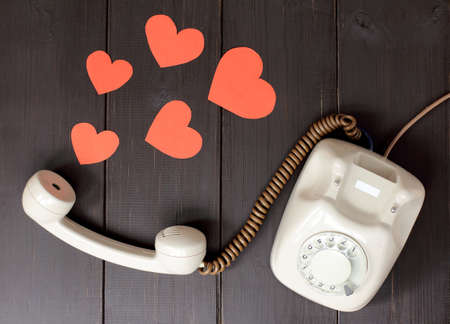 idea attractive voice in the form of hearts flying out of telephone handset lying on a wooden table / amorous talking by phoneの写真素材