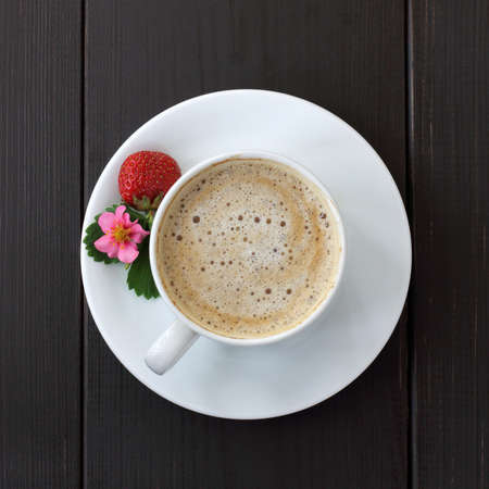 frothy coffee with decoration of berries, flower and leaf strawberries on a dark wooden background top view / coffee break with strawberry aromaの写真素材