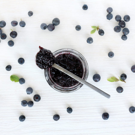 flat layout with blueberry berries strewn around the open the jar berry jam on a light wooden...