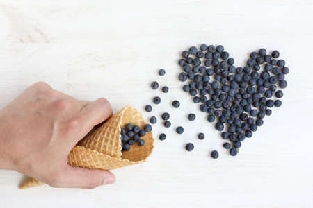 hand with waffle cones, from which poured the berries in a heart, top view / sweet Like followerの写真素材