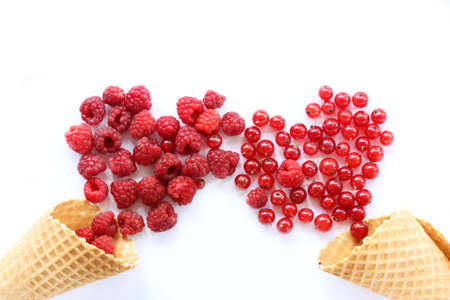 a plurality of raspberries and currants spill out of waffle cones in form of two red hearts / appetizing sweet loveの写真素材