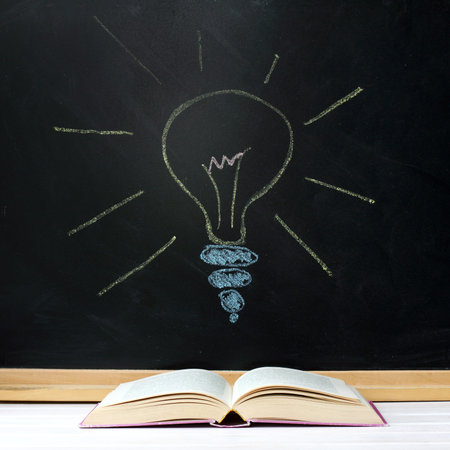 Opened book on background of blackboard and chalk drawn light bulb / searching for new ideas