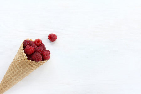 flat layout with waffle cup full of raspberries on a light wooden background top view / appetizing...