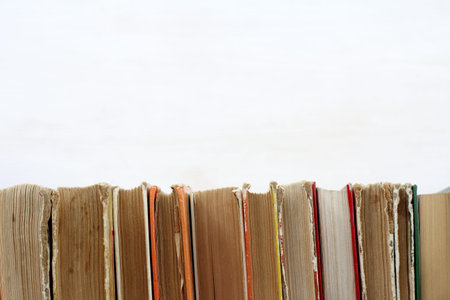 many old shabby books standing in a row on a light surface / used book shelfの写真素材