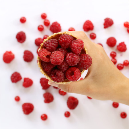 raspberries in a waffle cone, holding hand on the blurry background of red berries top view /...