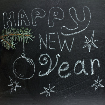 festive background with fir paw and inscription in chalk on a blackboard / happy new year