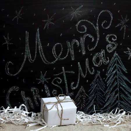 holiday gift on the background of congratulations drawn in chalk on a blackboard / standby Merry Christmasの写真素材