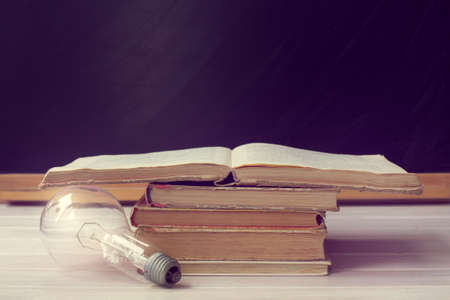 electric bulb lying close to a pile of old books on the background of blackboard / old ideas do not give lightの写真素材