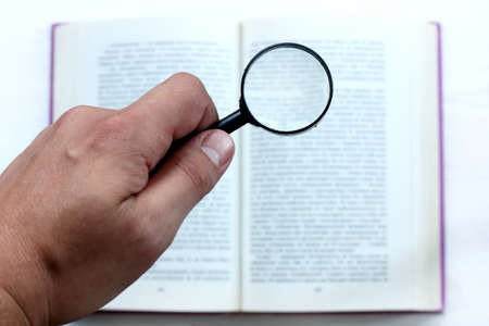 hand with magnifying glass on the background of an open book / thorough examination of informationの写真素材