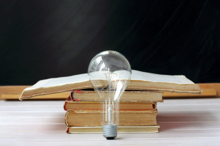 electric light bulb standing in front of an open book on the background of blackboard / waiting for...