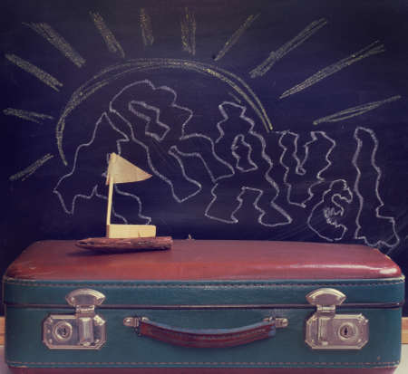 retro luggage and toy sailboat made with hands on a background of the drawn chalk sun / swim time vacationの写真素材