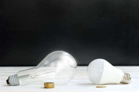Innovative and plain old light bulb with coins to pay for electricity against the darkness background / benefits of new technologiesの写真素材