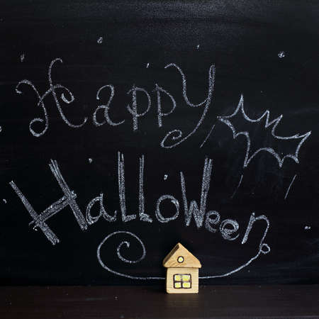 small house with a light in the windows on the background of signs drawn with chalk on blackboard / celebration of Halloween Nightの写真素材