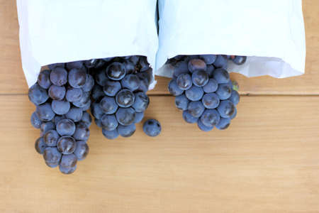 bunches of dark grapes lie in packages on a light wooden surface / crop of sweet berriesの写真素材