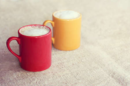 pair of colored mugs with frothy cappuccino stand on a desk / coffee for a couple with moodの写真素材