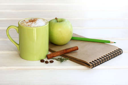 set of frothy cappuccino with cinnamon and apple, notebook, pencil / working environment in shades of greenの写真素材