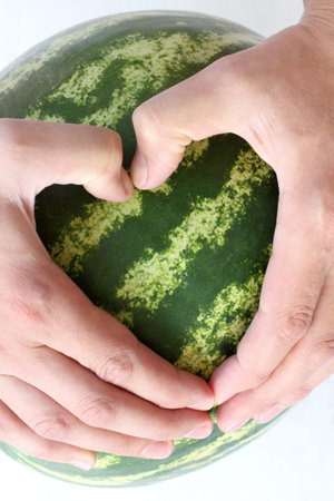 palms of hands stacked into a heart shape on a background of ripe watermelon / favorite striped sweet dessertの写真素材