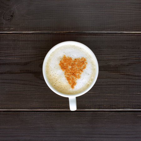 heart of cinnamon on foamy cappuccino in a white mug on a dark wooden background / favorite flavor...