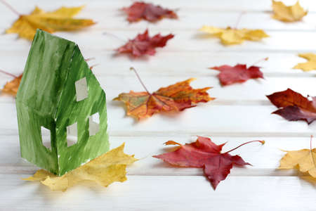 layout of the paper house painted in green, on a background of leaves / preparation for the autumn and winter seasonの写真素材