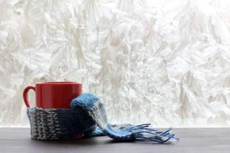 red mug wrapped a woolen scarf near a window decorations frost / winter warming drinksの写真素材