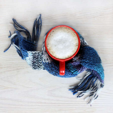 frothy cappuccino in the red circle wrapped in a blue scarf / warming drink for the winter holidaysの写真素材