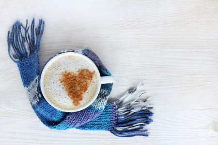red mug of coffee and a symbol of cinnamon hearts, wrapped in a blue scarf / warming atmosphere for loversの写真素材