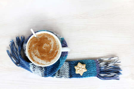 frothy cappuccino with cinnamon in a white cup, wrapped in a blue scarf top view / for prolonging the warming effectの写真素材