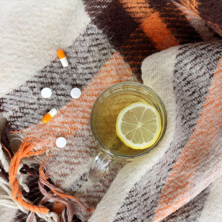 transparent cup of hot drink with lemon and drugs from the cold on warm plaid background / hot beverage for a speedy recoveryの写真素材