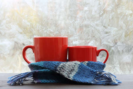 big and small red circle standing together in a blue scarf on the background of a frosty window / warming cozy atmosphere for breakfastの写真素材