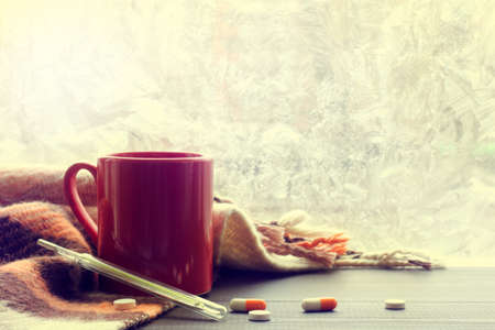 pellets tablets and mercury thermometer with red mug in blankets and background of frozen window / warming drinks for coldsの写真素材