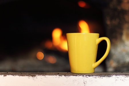 yellow ceramic mug is the old fireplace on the background of fire / warming atmosphere of home...