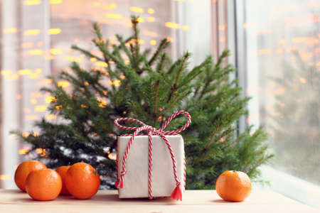 festive Christmas tree with gift and orange fruits on a background of light glare from windows / atmosphere of the new year meetingの写真素材