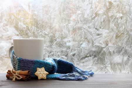 large white mug with blue scarf standing on a table with cinnamon and ginger cookies / warming drink on a winter dayの写真素材