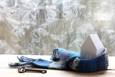 layout paper house in blue scarf and a key on a background of frozen window / warming technology in constructionの写真素材