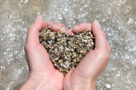 wet sea pebbles in the hands form a heart symbol on a background of water / declaration of loveの写真素材