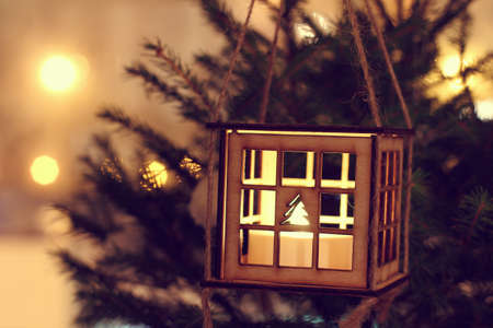 Wooden luminous lantern decorating this Christmas tree on the background New Year lights at night / cozy holiday atmosphereの写真素材
