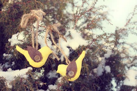 soft Christmas toys on a real green tree covered with snow / holiday bird on a branchの写真素材