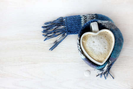 drop foamy cappuccino next to your favorite mug wrapped in a blue scarf / small cozy coffee breakの写真素材