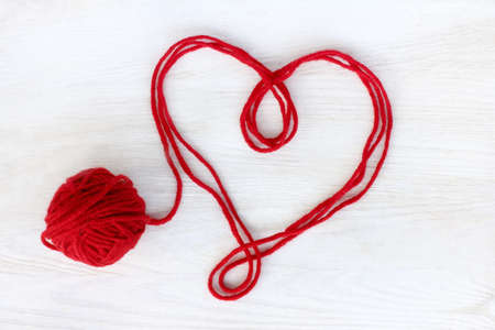 heart symbol of red thread on a light wooden surface top view / untied love affectionの写真素材