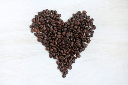 a lot of coffee beans in form of heart, on a light wooden table / coffee concept for Dating