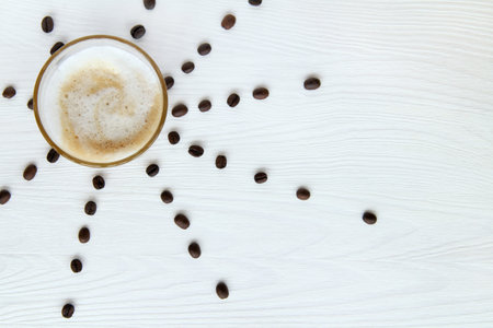 glass mug with a frothy cappuccino and coffee beans on the table / hot sunny drinkの写真素材