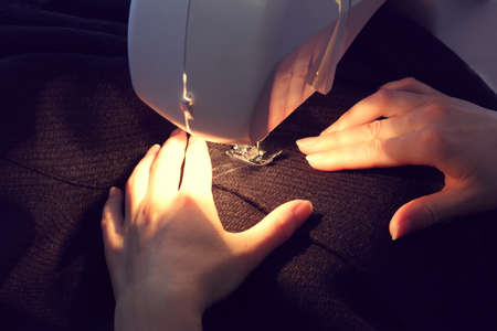 Seamstress sews details from dark fabric with a sewing machine / creation of fashionable clothesの写真素材