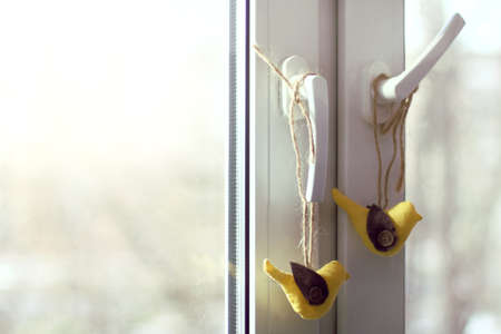 Pair of soft birds handmade against the background of a window / festive atmosphere of spring holidaysの写真素材