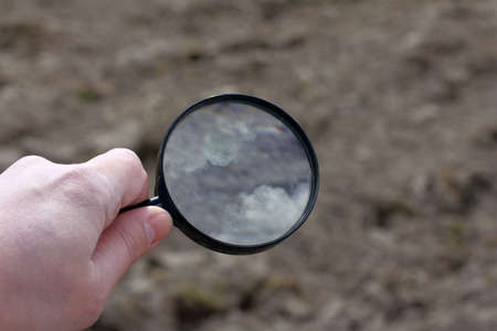 Hand with a magnifying glass with a reflection of the sky with clouds / search for solutionsの写真素材