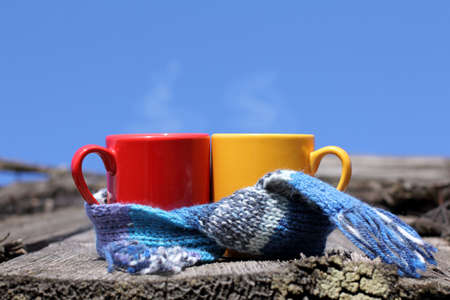 Red and yellow mug wrapped in a scarf against the sky / hot drinks in the fresh airの写真素材