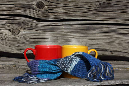 Red and yellow mug wrapped in a scarf on the background of a very old wooden surface / warming atmosphere near the houseの写真素材