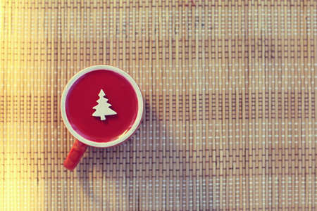 Inverted red cup with a Christmas tree symbol on a table background top view / Holiday wishes from the other sideの写真素材